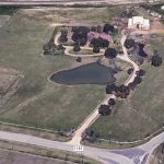 Aerial view of 2301 FM 1187 in Aledo, TX, showcasing a rural property with a house, pond, mature trees, fenced grassy areas, and a driveway leading from the road to the home amidst open land and outbuildings.