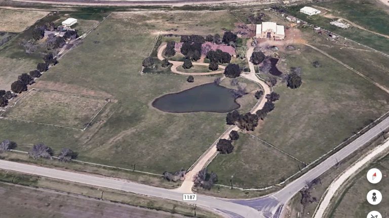 Aerial view of 2301 FM 1187 in Aledo, TX, showcasing a rural property with a house, pond, mature trees, fenced grassy areas, and a driveway leading from the road to the home amidst open land and outbuildings.