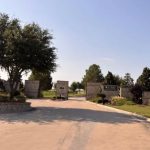 A gated community entrance at 972 San Jacinto Aledo TX 76008 features stone pillars, a driveway, manicured lawns, trees, and signage on the pillars under a clear blue sky.