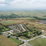 Aerial view of a suburban area with houses and green fields; a large plot of land is outlined in red, indicating its boundaries amid residential neighborhoods and open spaces.