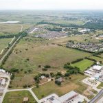 Aerial view of a semi-rural area with open fields, scattered houses, roads, a railroad track, and clusters of commercial and residential buildings surrounded by greenery.