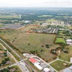 Aerial view of a large, grassy plot of land outlined in red, surrounded by residential neighborhoods, roads, and some commercial buildings in a suburban area.