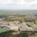 Aerial view of a rural town with a football stadium, school buildings, and open fields. A large area is outlined in red, indicating a specific property or parcel of land. Trees and scattered houses surround the area.