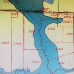 A digital map displaying numbered land parcels divided by red boundary lines, with a blue river or water body flowing through the center and some roads and smaller parcel divisions on the right side.
