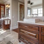 Spacious bathroom with wooden cabinets, marble countertops, two vessel sinks, large mirrors, tile flooring, a potted plant, and natural light coming through windows.