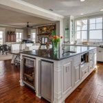 Bright, open kitchen and living area with wood floors, white cabinets, a large island with black countertop, vase of tulips, and large windows offering scenic outdoor views.