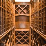 Wooden wine cellar with empty racks and diamond-shaped shelves, viewed from the entrance. The shelves line both walls and the back, creating a warm, organized storage space with ample slots for wine bottles.