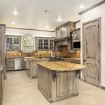 Spacious kitchen with light wood cabinets, granite countertops, a central island, stainless steel appliances, tiled floor, and an arched window above the sink letting in natural light.