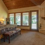 Cozy bedroom with a rustic wooden bed, decorative stars on the wall, a stone fireplace, and large windows letting in natural light with a view of trees outside.