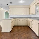 Spacious vintage kitchen with cream cabinets, silver hardware, gray countertops, parquet wood flooring, double sinks, pendant lights, and large windows providing ample natural light.