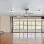 Spacious living room with wood flooring, built-in shelves, stone fireplace, ceiling fan with lights, and large sliding glass doors leading to a sunroom and backyard view.