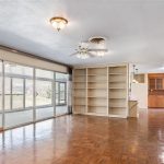 Spacious living room with wood parquet flooring, built-in shelves, ceiling fan, and sliding glass doors leading to a screened porch; open layout connects to kitchen and dining areas.