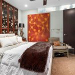 Elegant bedroom with Asian-inspired black lacquer wall panels, a large white bed with plush pillows, a brown fur throw, vintage-style furniture, and a bold orange abstract painting on the wall.