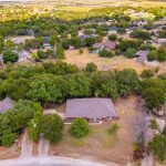 Aerial view of a suburban neighborhood with scattered houses surrounded by trees and greenery, set in a rural landscape with roads winding through the area.