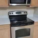 A modern kitchen features a stainless steel electric stove with an oven and a matching microwave above it, surrounded by light wood cabinets and white countertops.