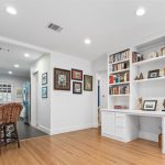Bright, modern kitchen with turquoise cabinets and patterned tile island, adjacent to a built-in white bookcase and desk, wood flooring, and colorful framed art on the walls.