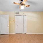 A simple, empty room with light yellow walls, wood flooring, a ceiling fan with a light, a closed white closet, an open door, a small window, and a wall hook rack near the door.