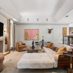 A spacious, modern living room with a large sectional sofa, a lit fireplace, wall-mounted TV, eclectic artwork, and animal sculptures; neutral tones and abundant natural light create a cozy, stylish atmosphere.
