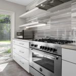 Modern kitchen with stainless steel stove and oven, sleek gray and white cabinetry, microwave, glass shelves, and large windows overlooking a backyard with a swimming pool and greenery.