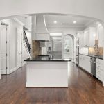 Modern kitchen with white cabinets, stainless steel appliances, a central island with a black countertop, hardwood floors, and arched doorways, all in a bright, open space.