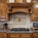 A kitchen with wooden cabinets, granite countertops, a gas stove, a toaster oven, a set of knives, and various utensils. The backsplash features a decorative tile pattern with a small framed piece in the center.