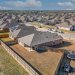 Aerial view of a suburban neighborhood with rows of houses, fenced backyards, and a trampoline in one yard under a partly cloudy sky.