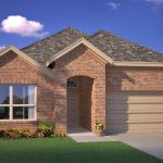 A single-story brick house with a two-car garage, large front window, and manicured lawn with shrubs and flowers, set against a blue sky with a few clouds.