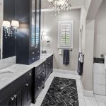 Elegant bathroom with dual sinks, black cabinets, marble countertops, tiled floors, a chandelier, white bathtub, and towels neatly hung on racks, with natural light coming through a plantation-shuttered window.