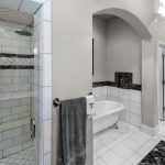 Modern bathroom with a glass-enclosed shower, white tile walls, a freestanding bathtub, black and white tile accents, a towel hanging on a ring, and a chandelier on the ceiling.
