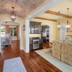 Bright, open dining and kitchen area with wooden floors, exposed ceiling beams, brick arched ceiling, and elegant lighting. Neutral decor with a rustic dining table, cushioned chairs, and light yellow walls.
