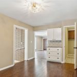 A small room with tan walls and dark wood flooring, featuring a ceiling light, a doorway to a brick-walled area, a white cabinet with drawers, and two open doors leading to other rooms.