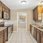 A kitchen with dark wooden cabinets, granite countertops, stainless steel appliances, and a double sink. The floor is tiled, and there is a window above the sink with natural light coming in.