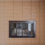 A brown brick fireplace with a black metal framed glass door, set against a beige wall in a room with wooden flooring.
