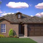 A single-story brick house with a gabled roof, a small dormer, two-car garage, and neatly trimmed bushes and flowers in the front yard under a blue sky with scattered clouds.
