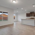 Open-concept kitchen and living area with light wood flooring, white walls, large window, recessed lighting, and a kitchen with dark cabinets, granite countertops, and stainless steel appliances.